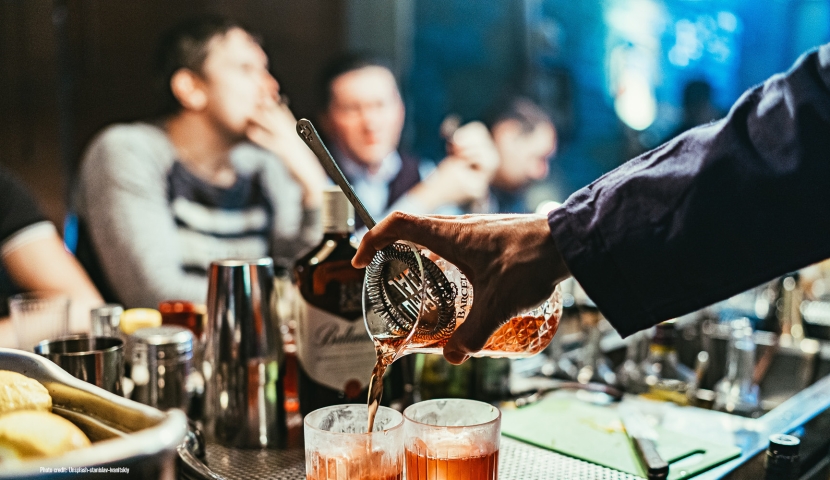 Man pouring drinks at a crowded bar. Photo credit: Unsplash-stanislav-ivanitskiy